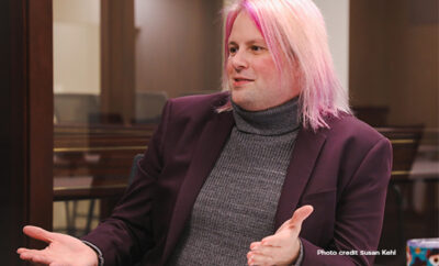 Open hand jesture by a person with pink hair and a dark blazer